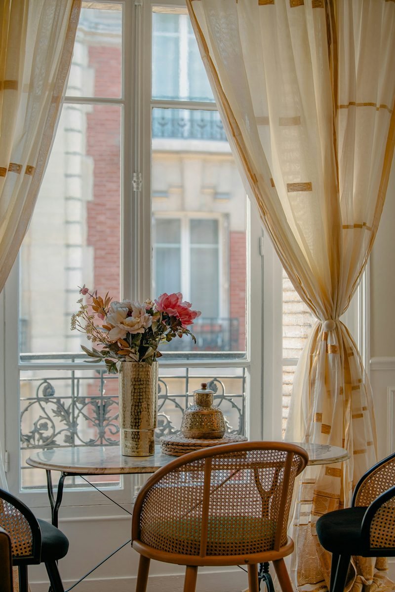 Table et bouquet de fleurs devant une porte-fenêtre à balcon en fer forgé dans un appartement parisien
